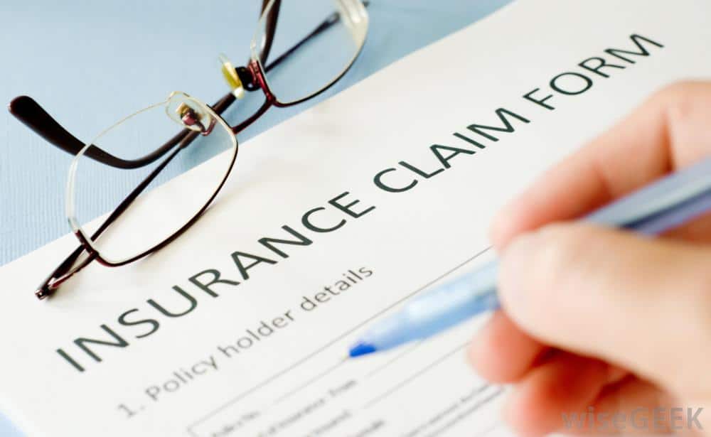 The image shows a hand holding a pen, in the process of filling out an insurance claim form.